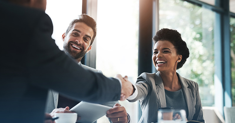 Business woman smiling and shaking hands with male