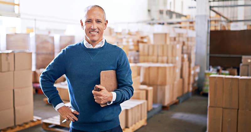 Happy business owner in warehouse holding clipboard