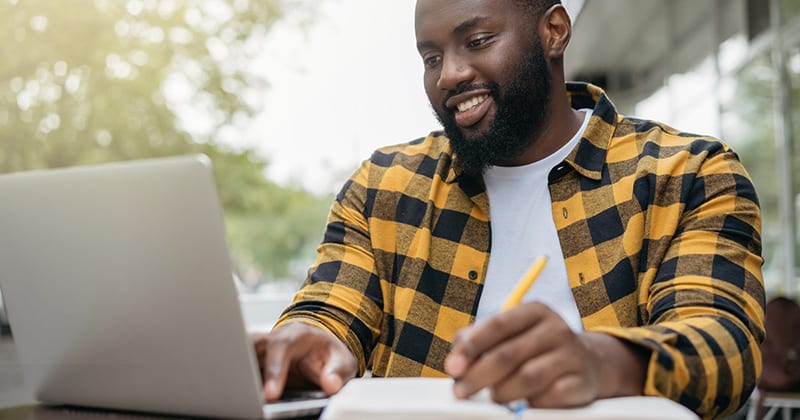 Man taking notes and looking at laptop