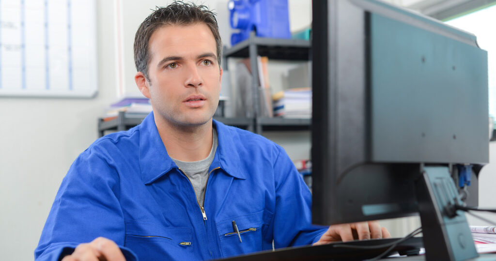 Man in blue jumpsuit sits behind computer