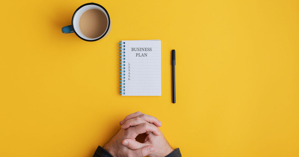 Spiral notebook and pen on yellow background with business plan ideas