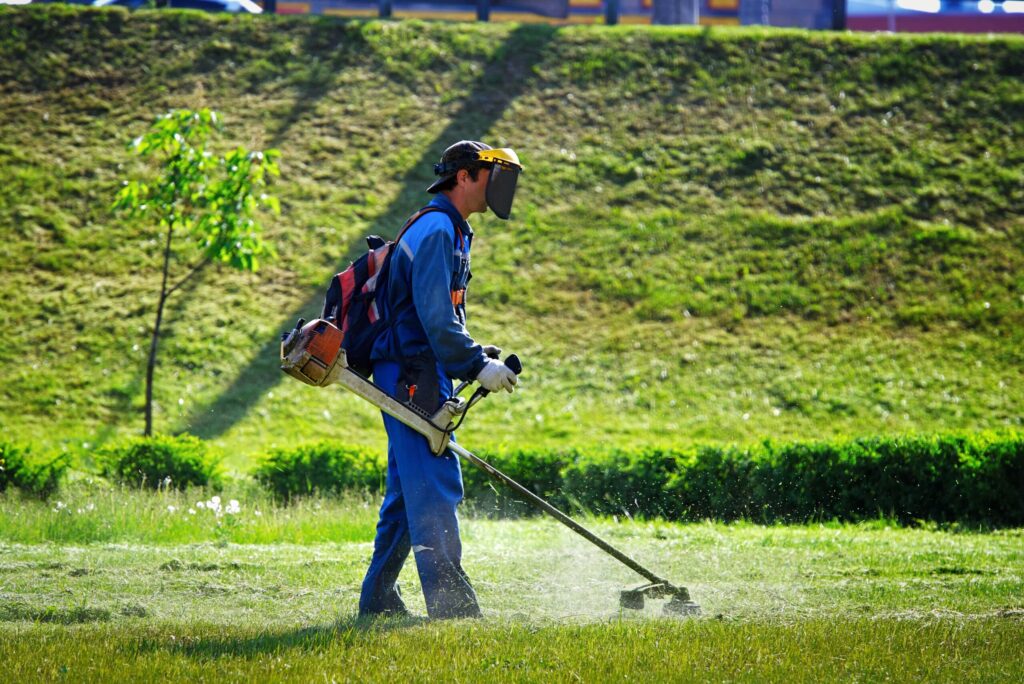Lawn care company employee mowing the grass with lawn mower in the park.