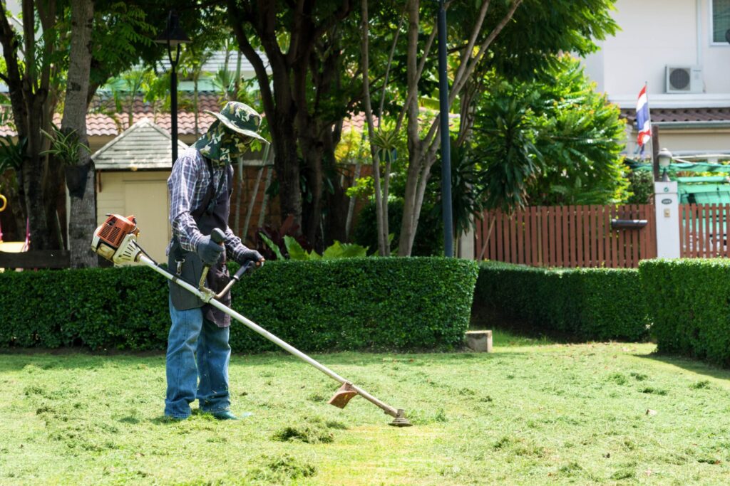 A gardener mowing grass with a string lawn mower.