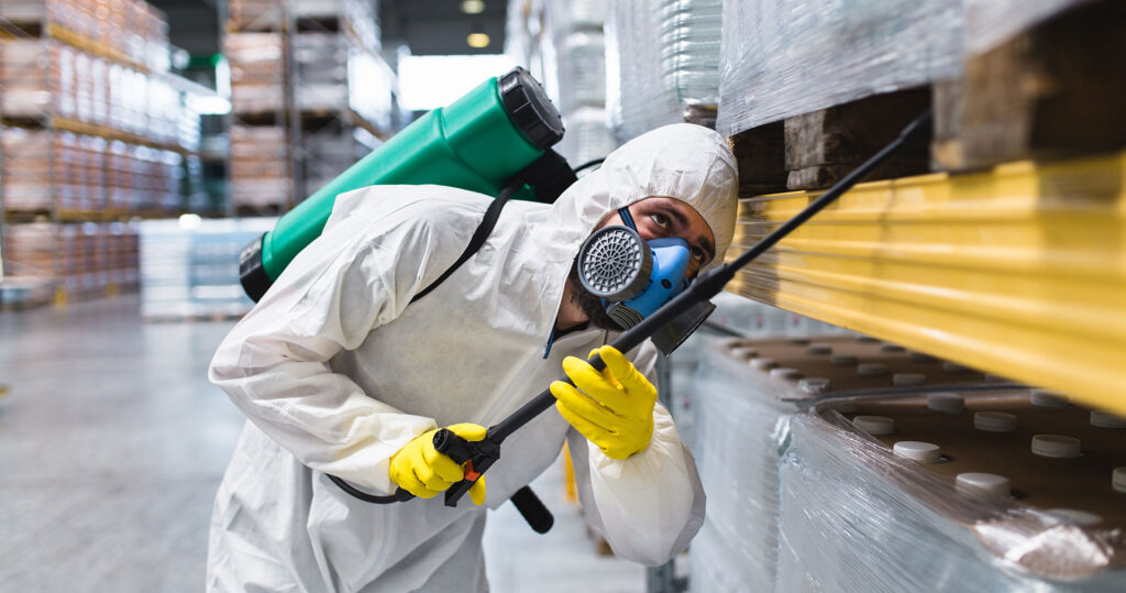 Pest-control-technician-in-white-suit-spraying-commercial-warehouse